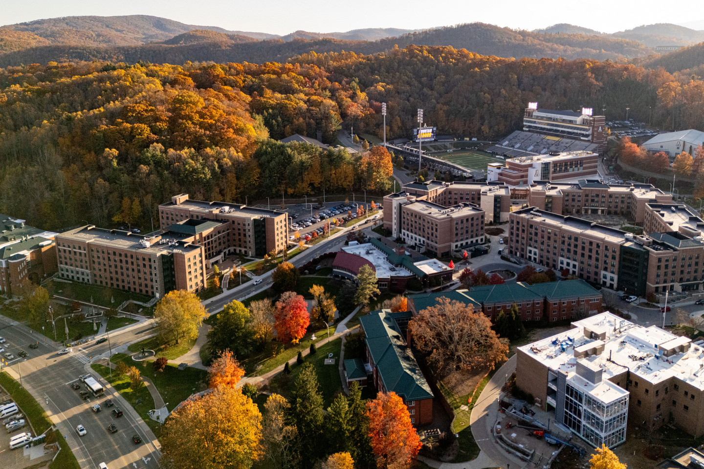 Aerial view of App State campus with stadium and buildings surrounded by colorful autumn trees and hills.
